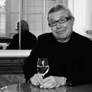 Foto von Daniel Liebeskind mit einem Glas in der Hand und einem Spiegel im Hintergrund
