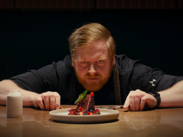 Koch schaut akribisch auf einen Dessertteller, der vor ihm steht.
