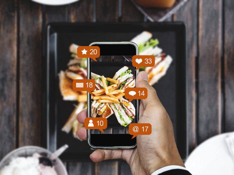 Handy macht ein Foto von dem Essen, welches auf einem Tablet dadrunter liegt